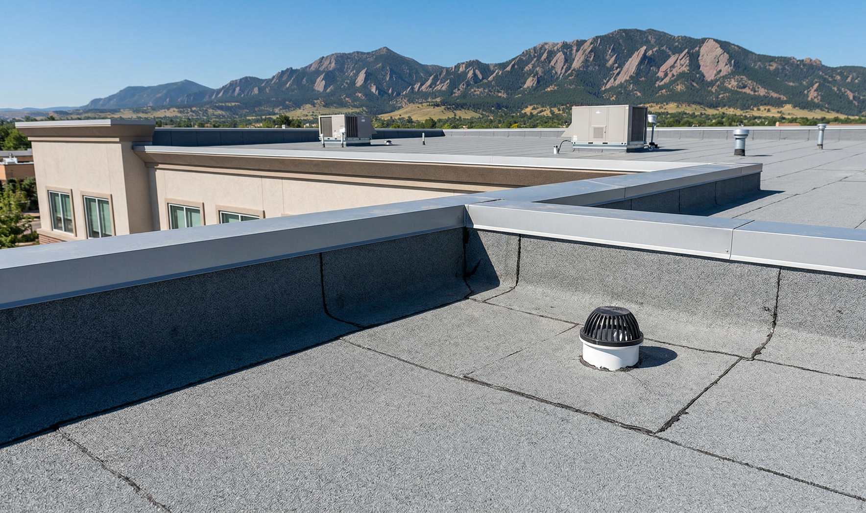 A flat commercial rooftop with a gray granulated membrane, a small circular roof vent, and mountains in the distance.