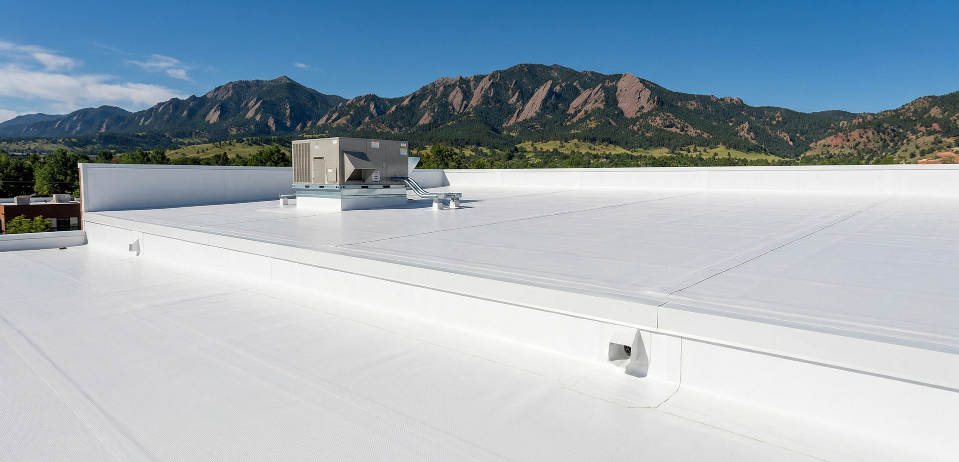 A white industrial roof with an HVAC unit, featuring a view of mountains under a clear blue sky.
