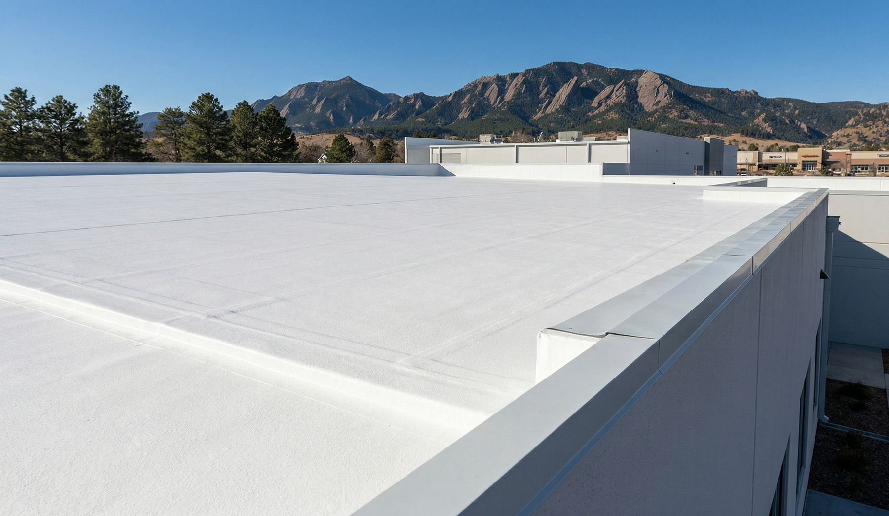 A bright white, flat rooftop with a metal parapet wall, overlooking distant mountains under a clear blue sky.