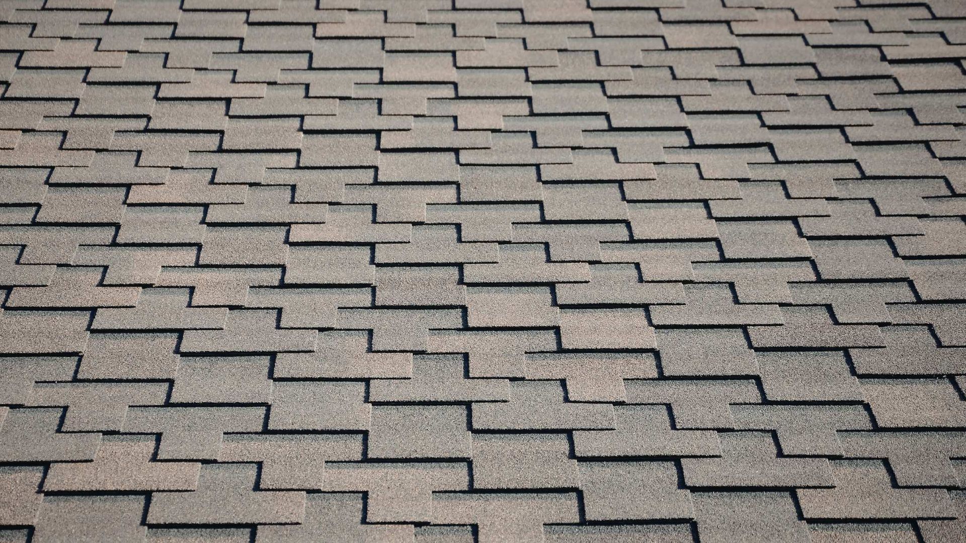 A full-frame view of gray, textured architectural shingles on a roof, arranged in a repeating, staggered zigzag pattern.