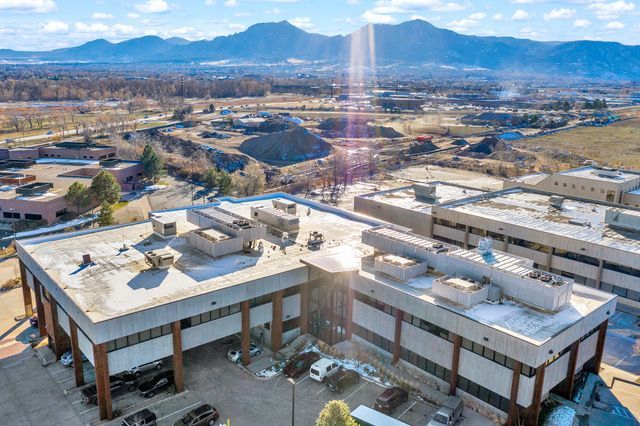 An aerial view of a multi-story office building with flat roofs and brown support pillars, set against distant mountains.