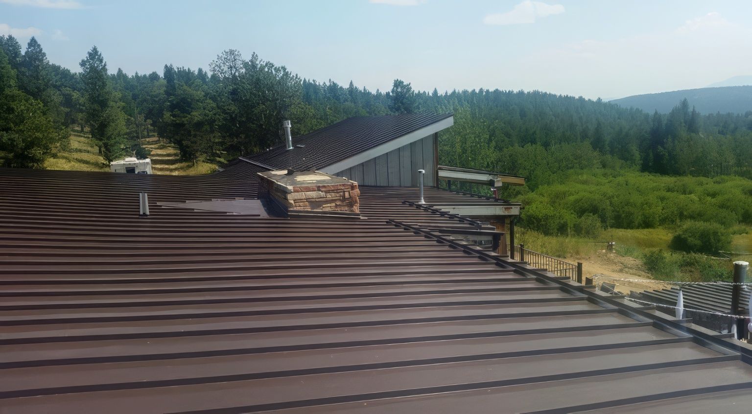 A brown metal roof slopes downward toward a wide, scenic vista of green pine forests and rolling mountains.