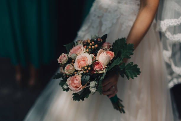 Bride in white dress holding a bouquet of pink roses and greenery.
