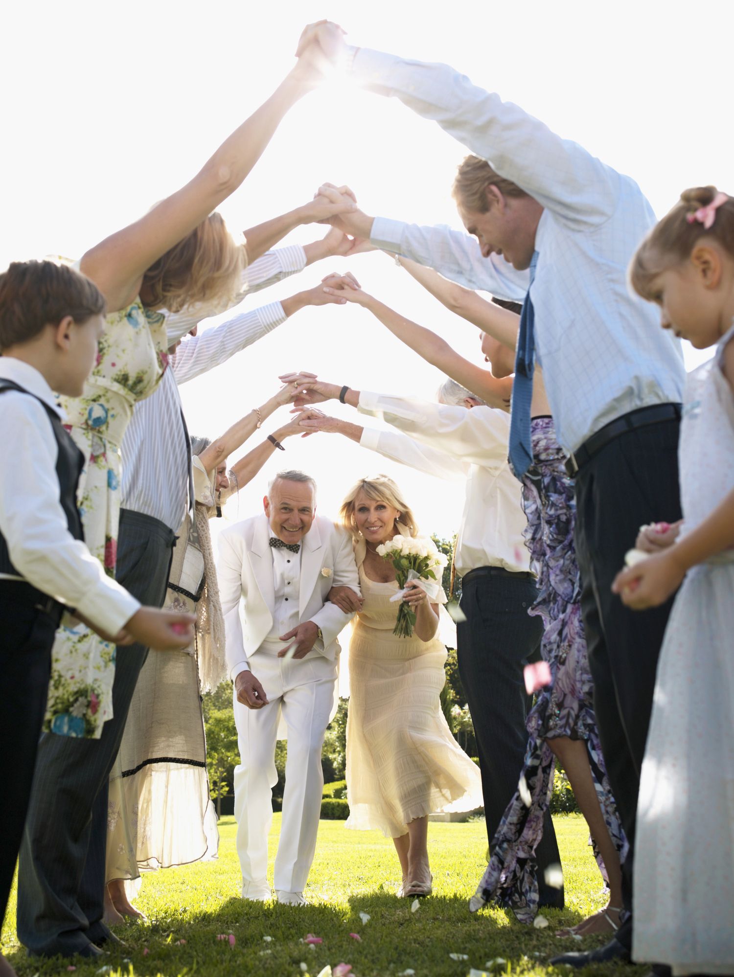 Wedding couple walks under an archway of raised arms held by guests on a sunny day.