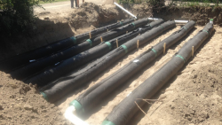 A trench showing an installed septic drain field system with parallel black drainage pipes connected by white PVC.