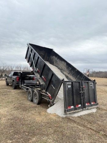 A dumpster is being pulled by a truck in a field.