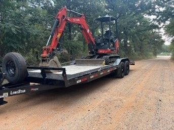 An excavator is sitting on top of a trailer on a dirt road.