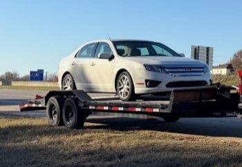 A white car is sitting on top of a trailer.
