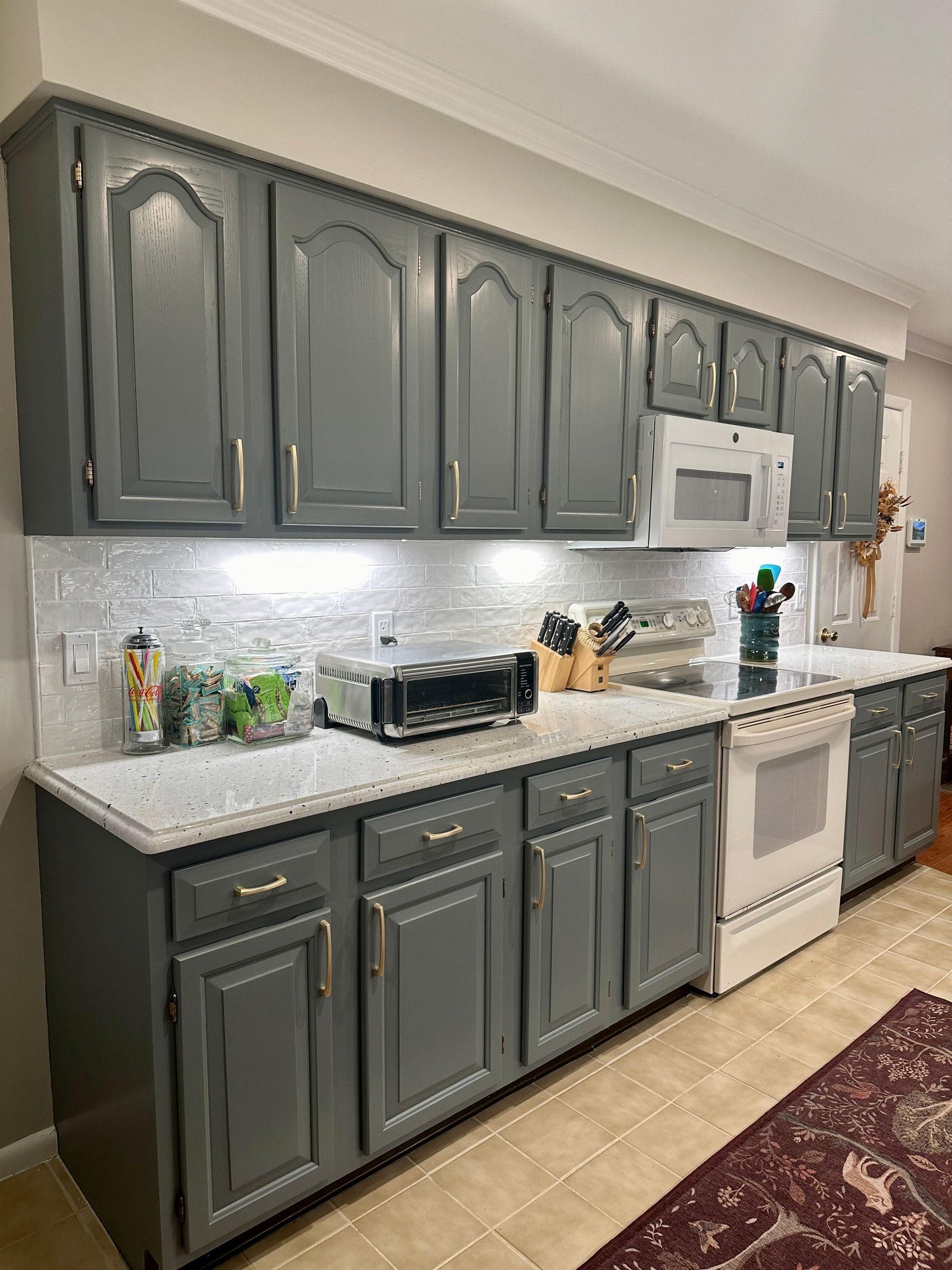 Gray kitchen cabinets with white countertops, white appliances, and under-cabinet lighting.