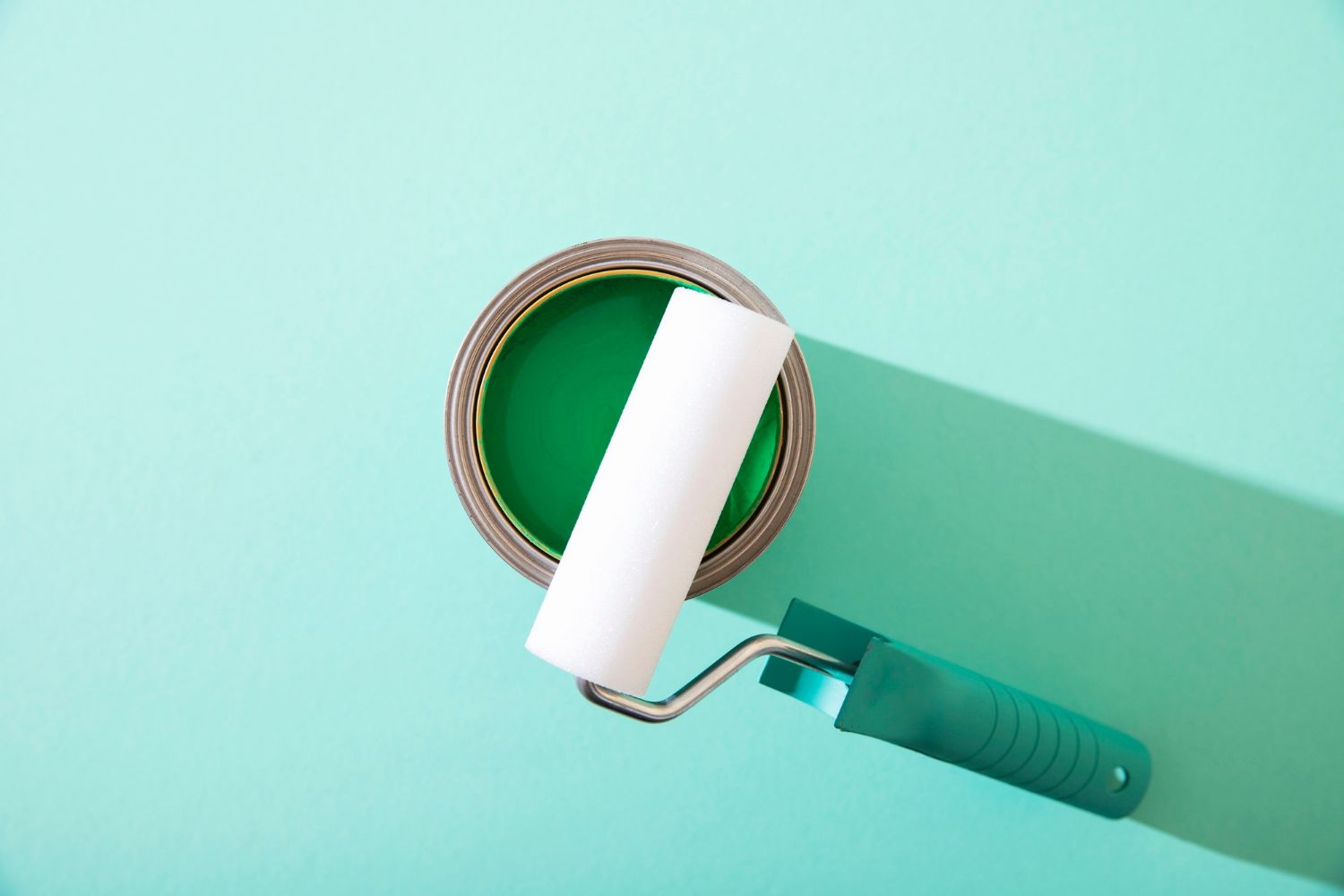 A can of green paint and a paint roller on a blue wall.