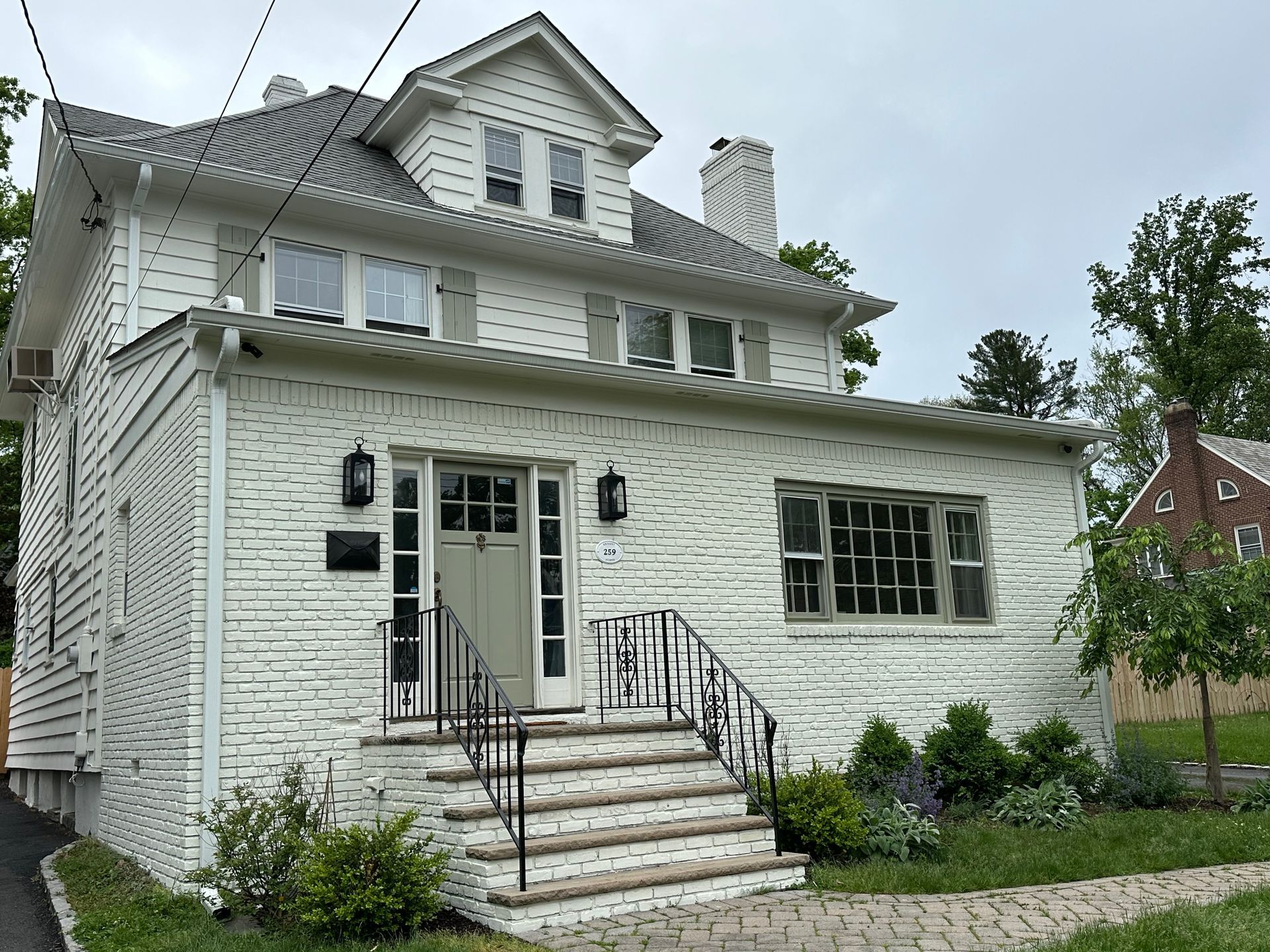 White-painted brick house with a gray roof, black railing, and sage green door.