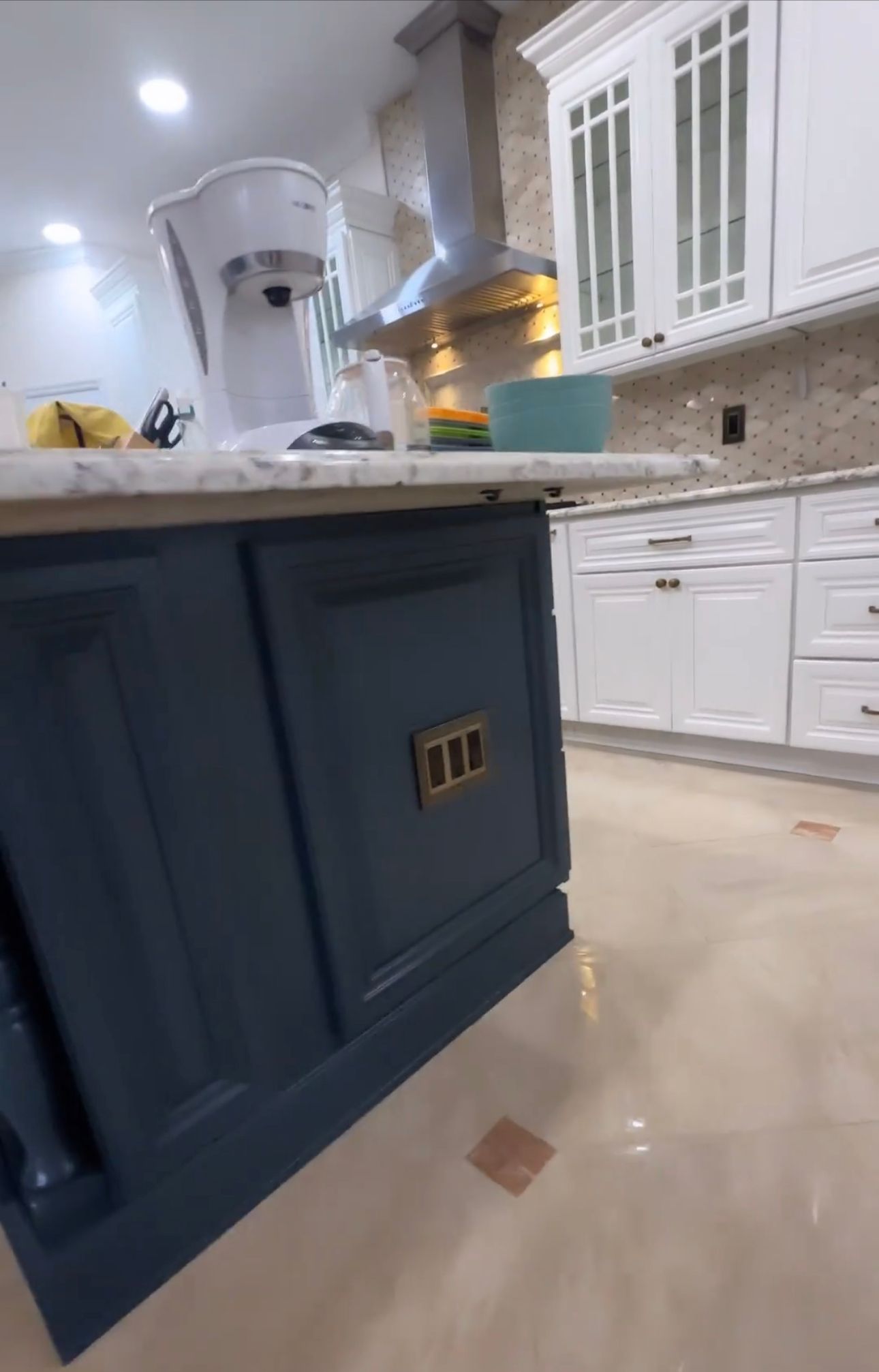 Blue kitchen island with gold hardware; white cabinetry, and stainless steel hood.