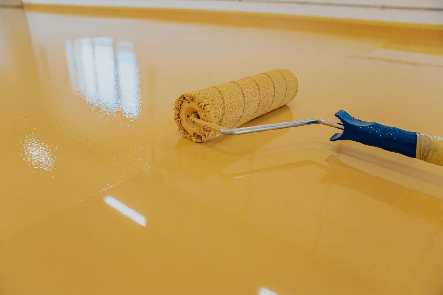 Yellow epoxy floor being applied with a paint roller in a room.