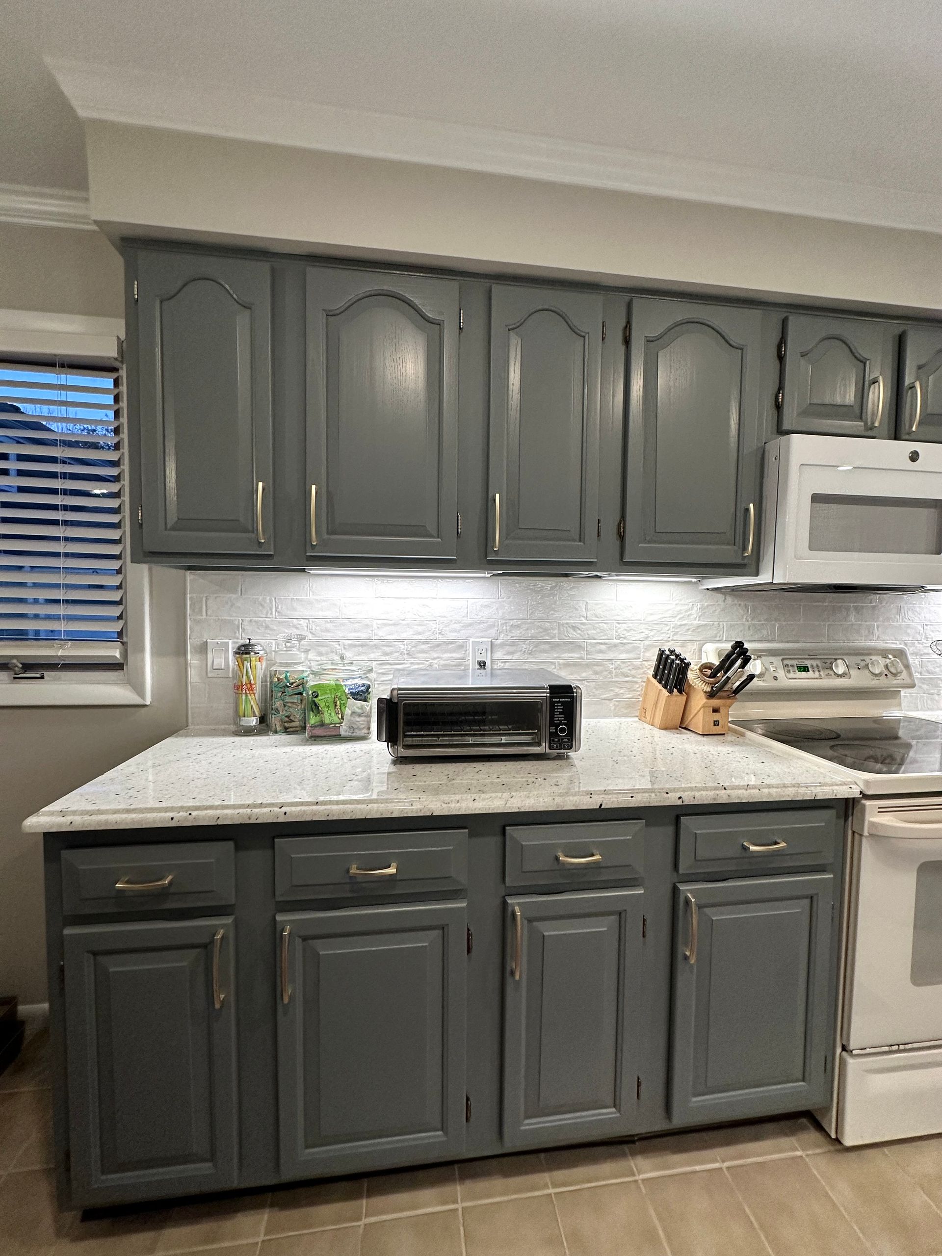 Gray kitchen cabinets with gold hardware and white countertops.