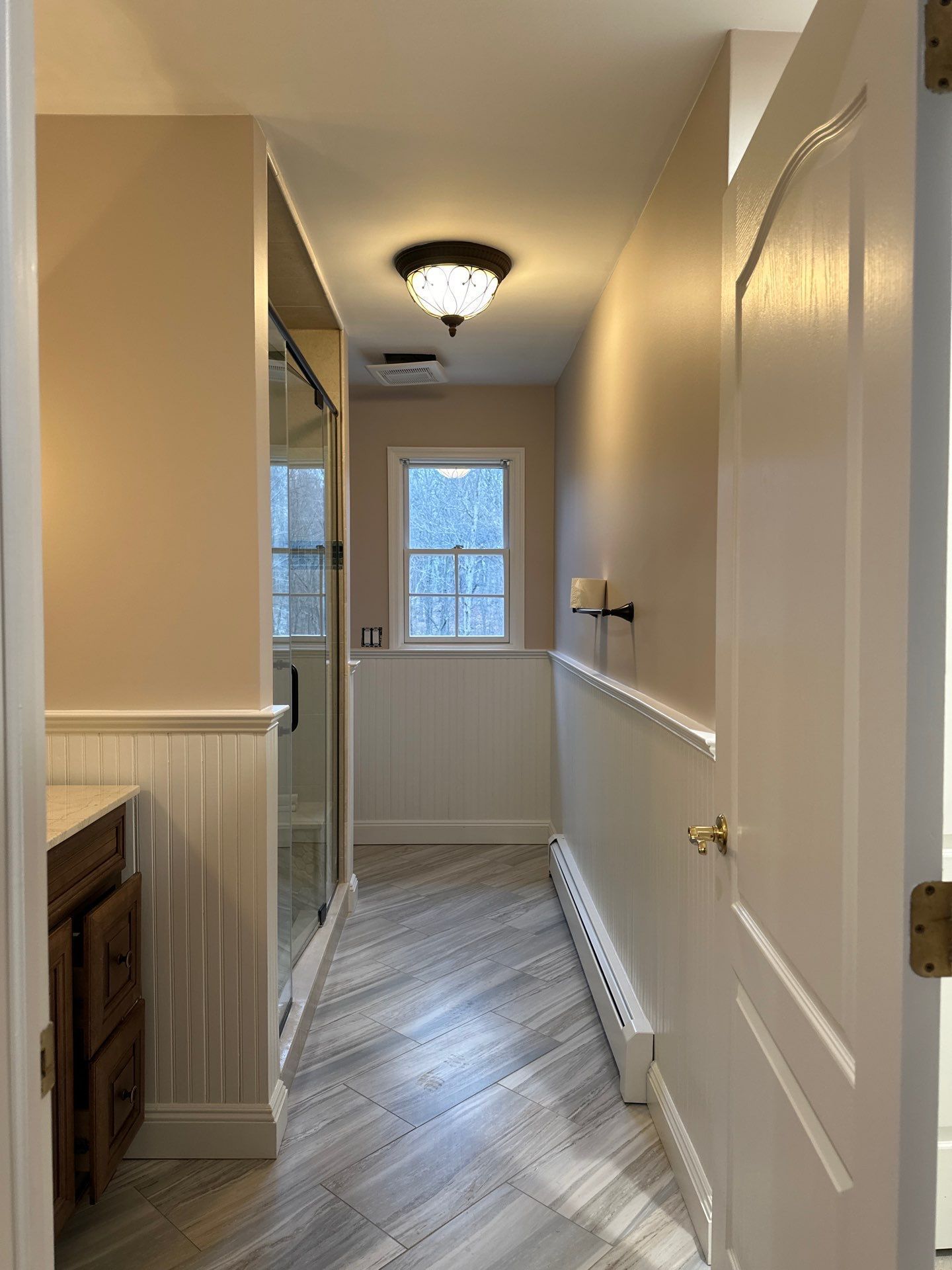 Narrow bathroom with light-colored walls, wood trim, and a shower on the left.