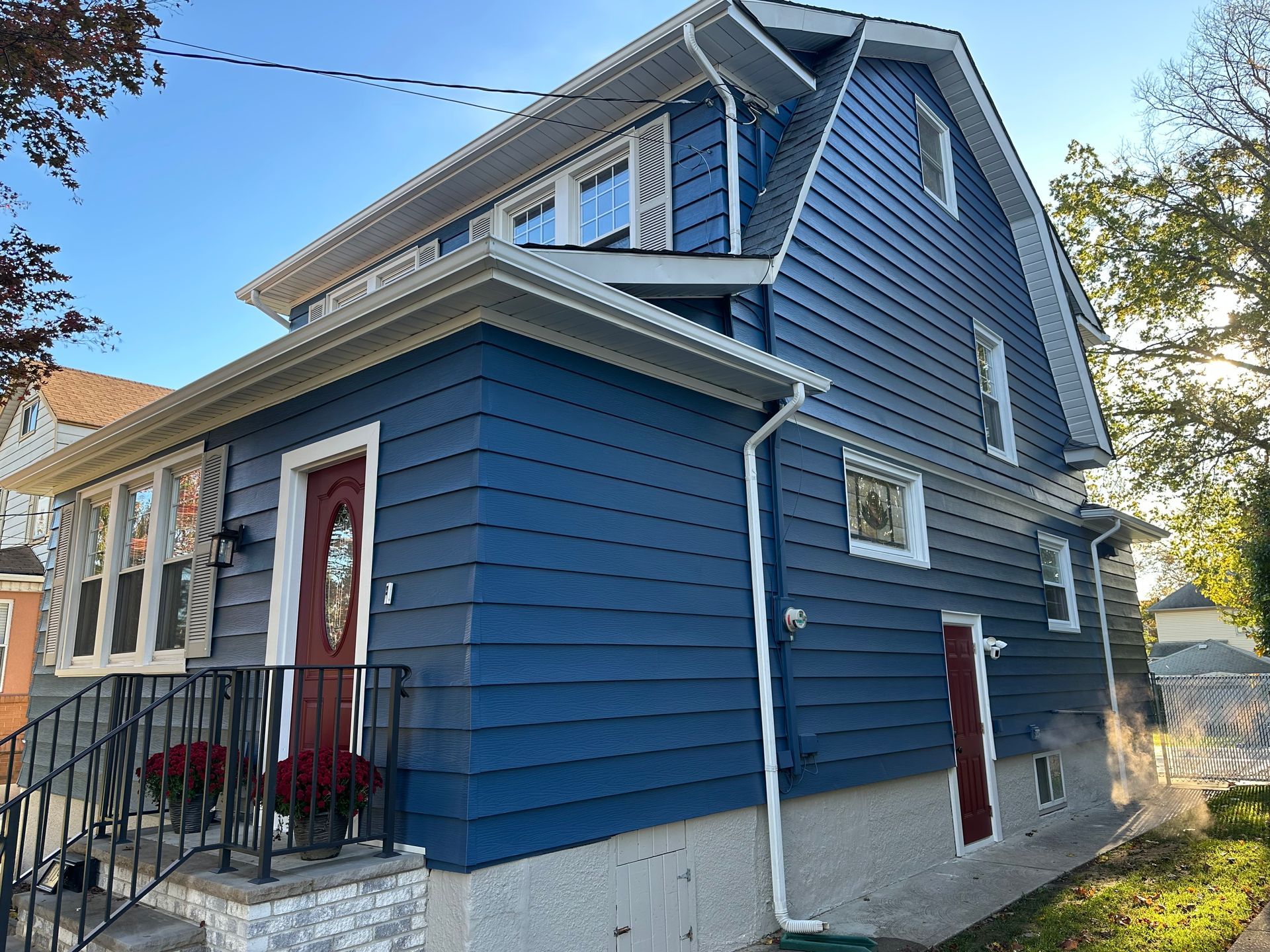 Blue house with red doors and white trim, front porch, and black railing against a blue sky.