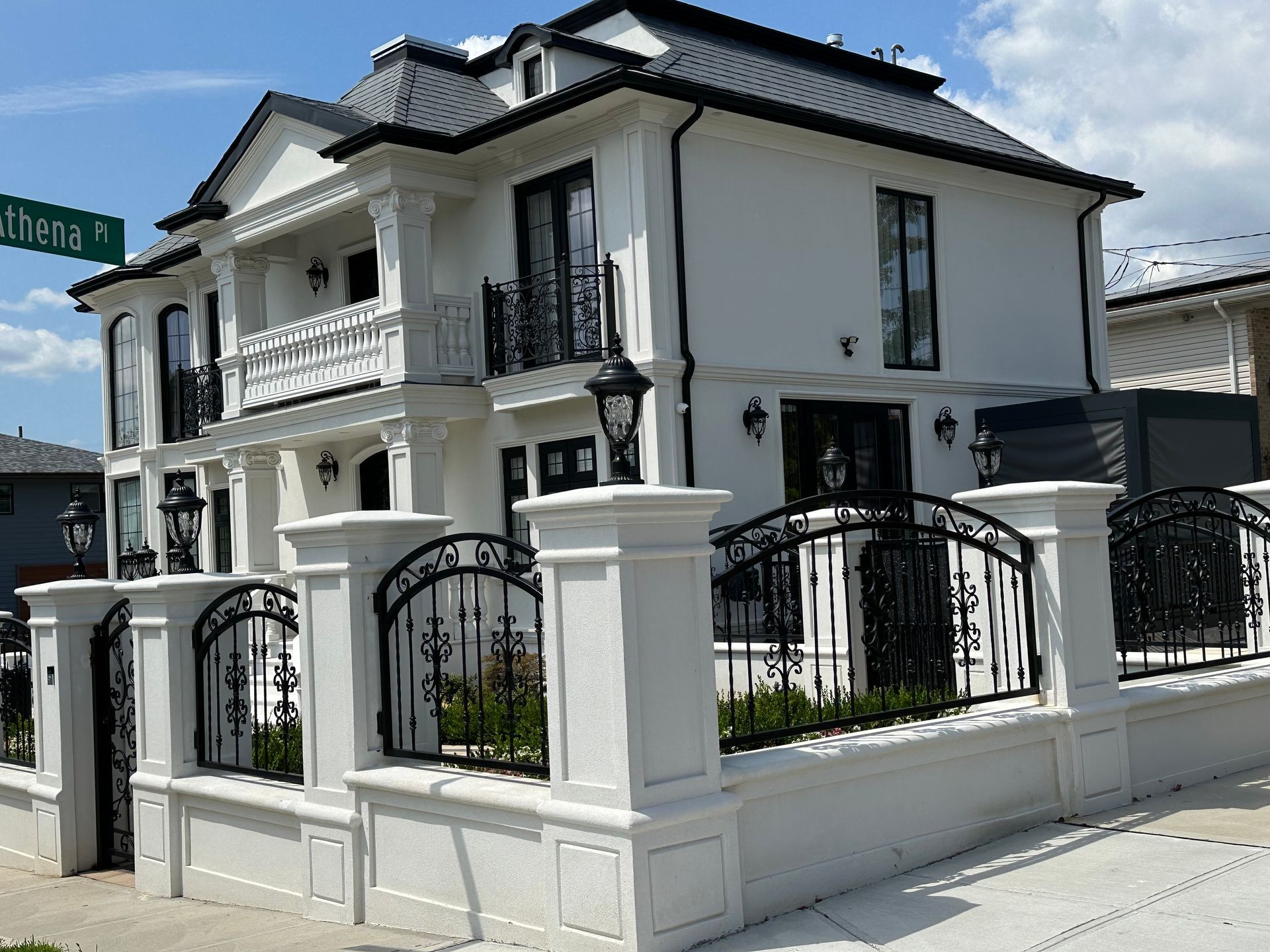 White two-story house with black roof and iron fence on a street corner