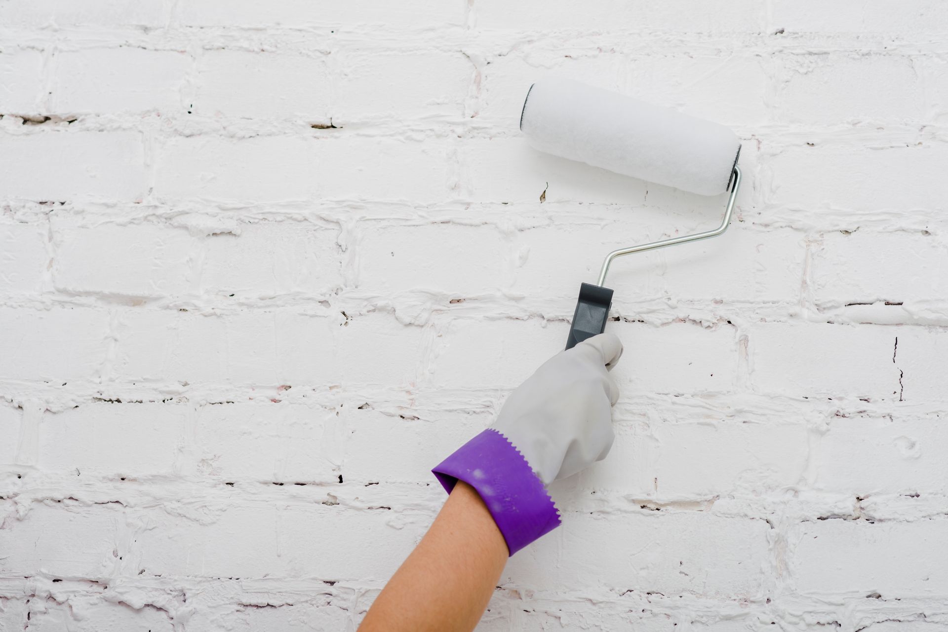 A person is painting a white brick wall with a paint roller.