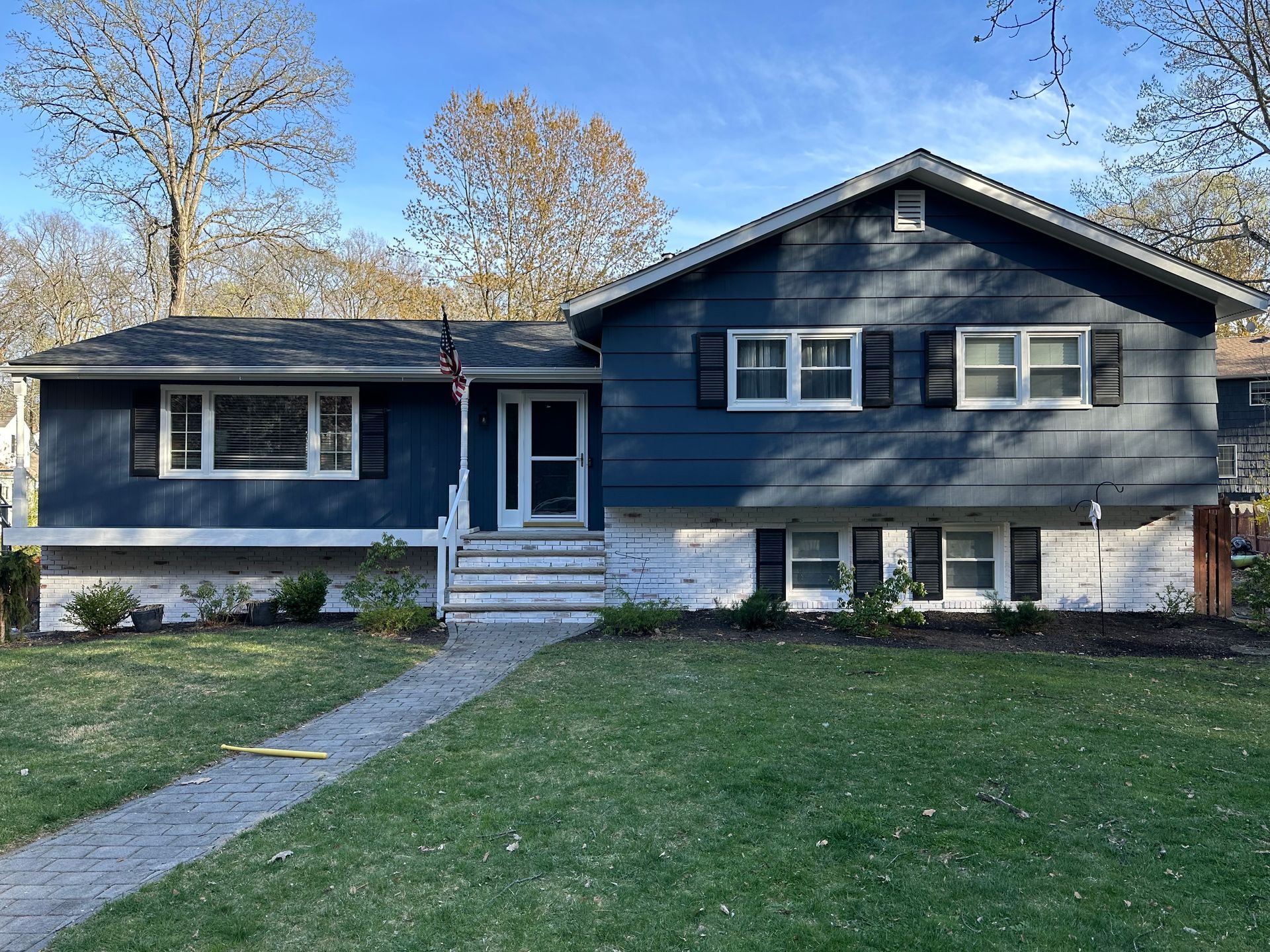 A two-story blue house with black shutters, a walkway, and a green lawn.