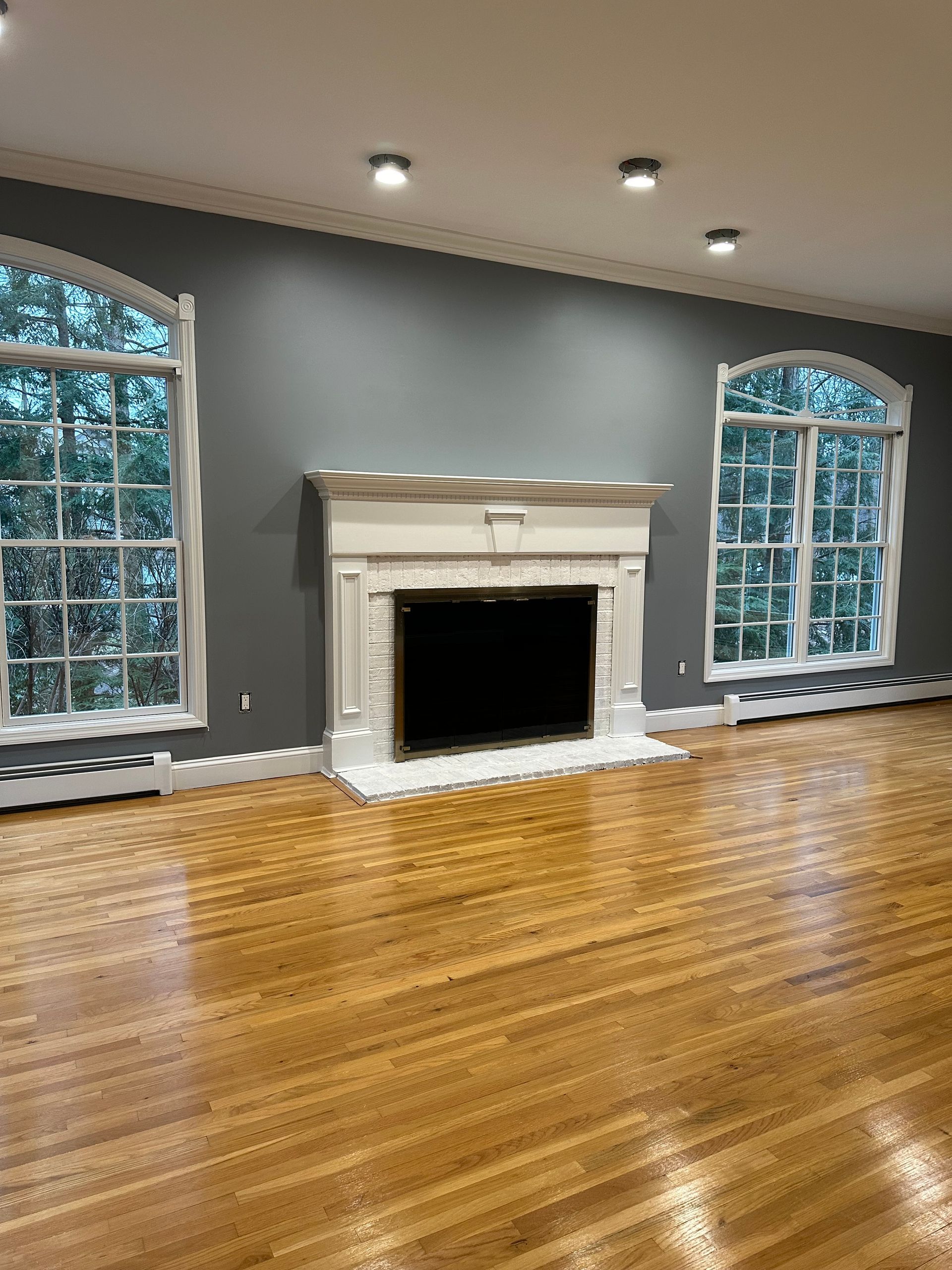 Living room with a fireplace, arched windows, and wood floors. Gray walls, white trim.
