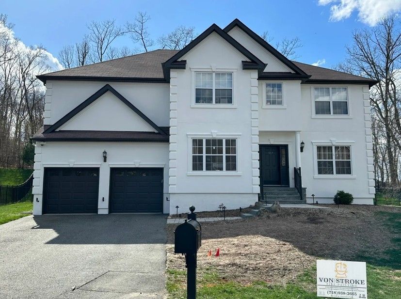Two-story white house with dark accents and garage doors. Black mailbox and driveway in front of a grassy lawn.