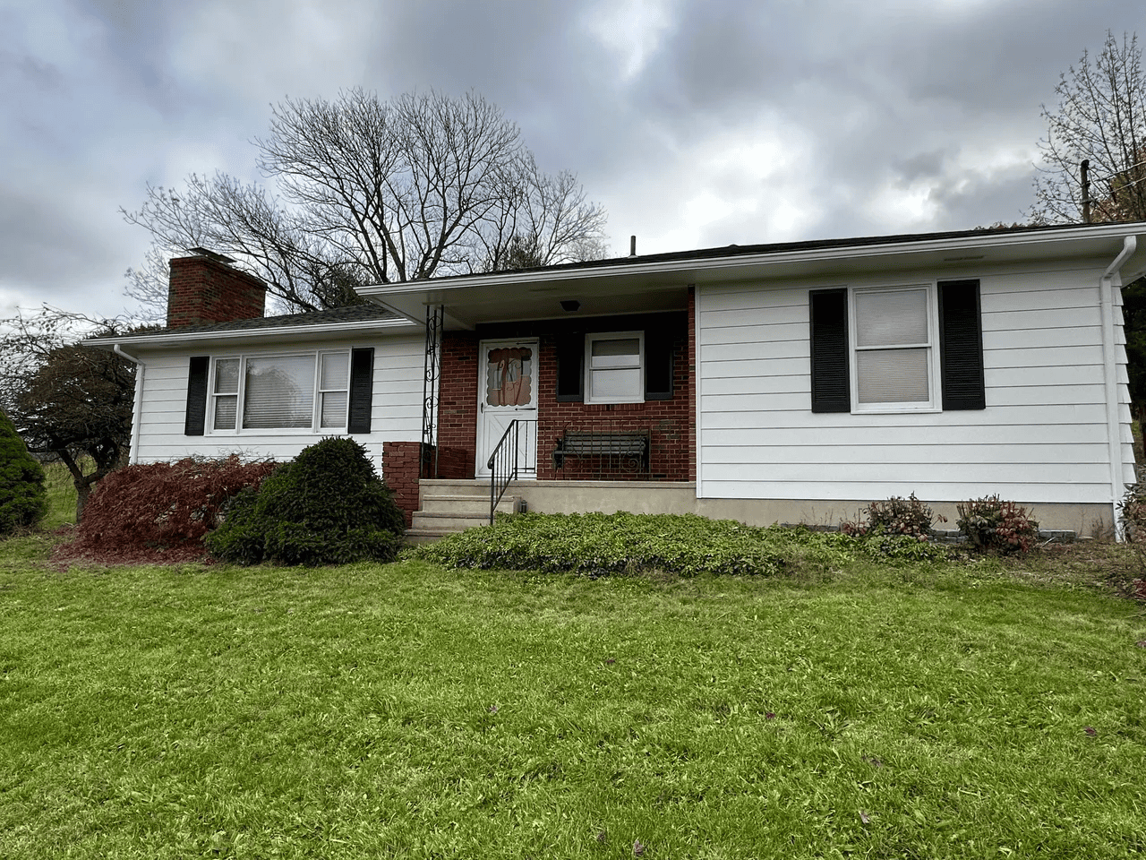 A white house with black shutters is sitting on top of a lush green field.