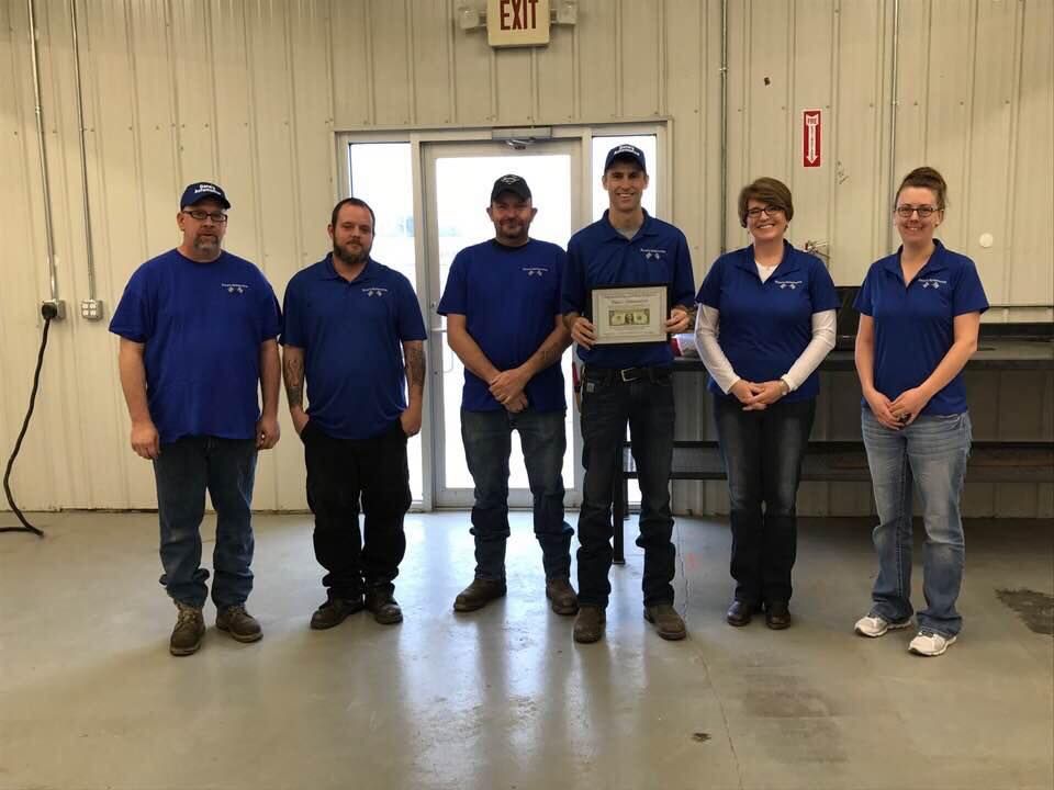 Street scene at dusk with brick buildings, streetlights, and a flag pole under a colorful sky.
