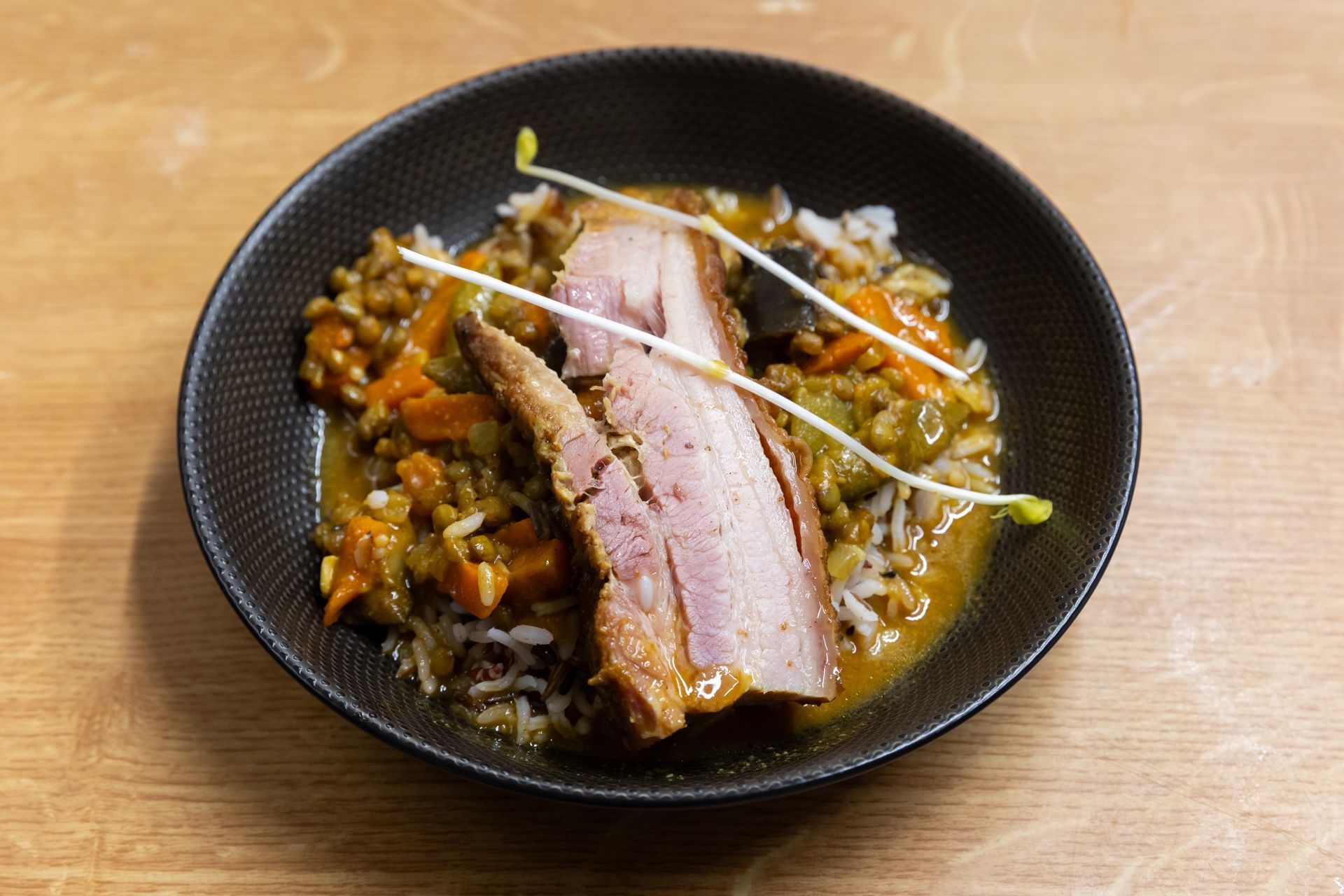 Un bol noir rempli de viande et de riz sur une table en bois.