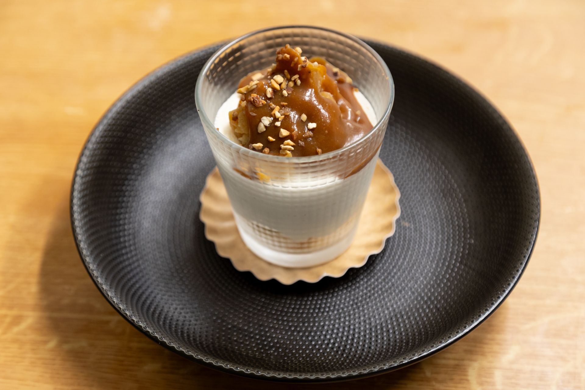 Un dessert dans un verre sur une assiette noire sur une table en bois.