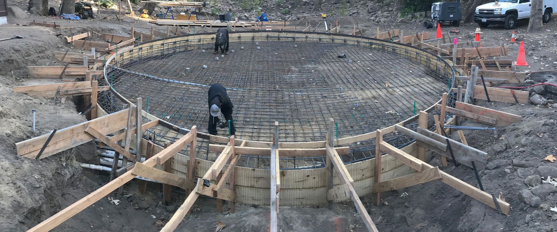 Construction site of a circular foundation with rebar and wooden supports, a worker is visible.