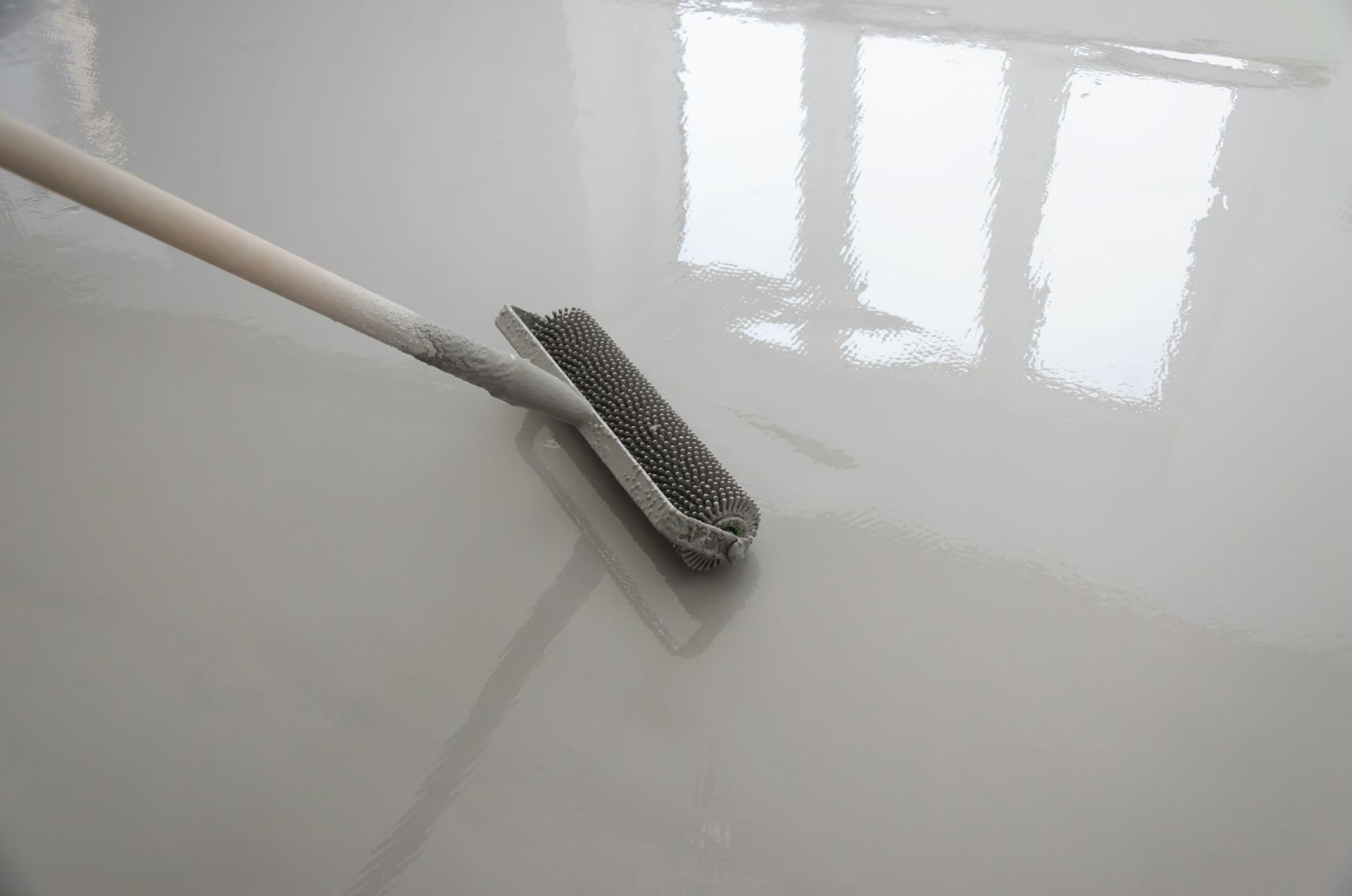 A floor being smoothed with a squeegee, reflecting light from a window.