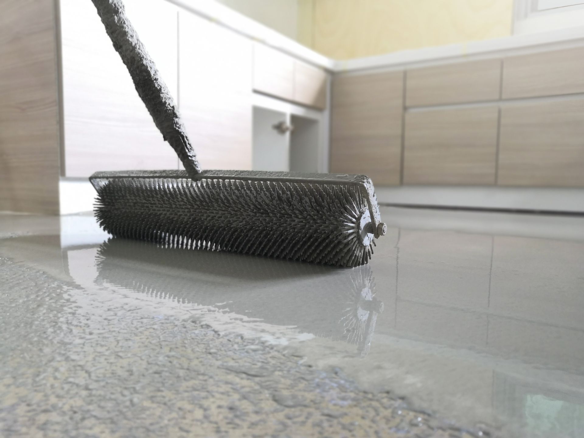 Black spiked roller smoothing gray epoxy flooring in a kitchen.