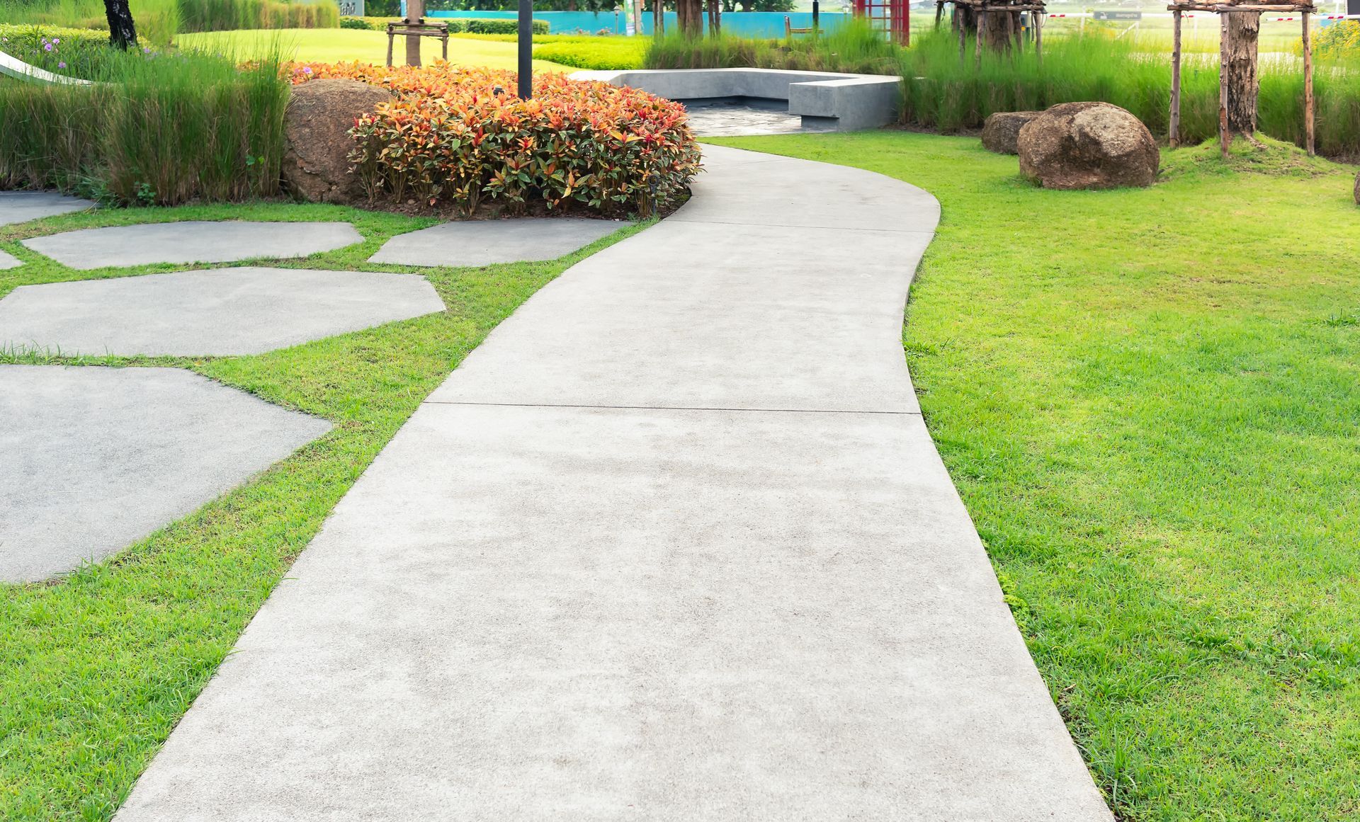 Curving concrete pathway through a green lawn, edged with grass and stone stepping stones.