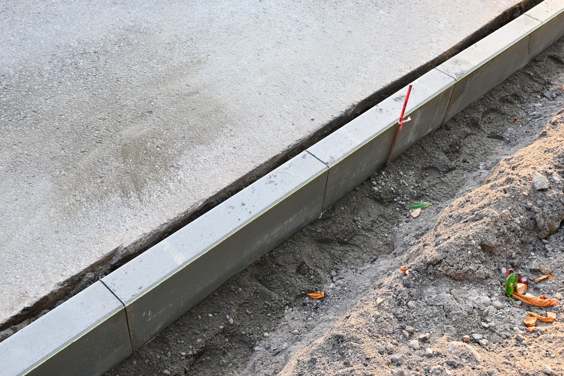 Concrete curb bordering a paved surface with dirt and debris on the right.