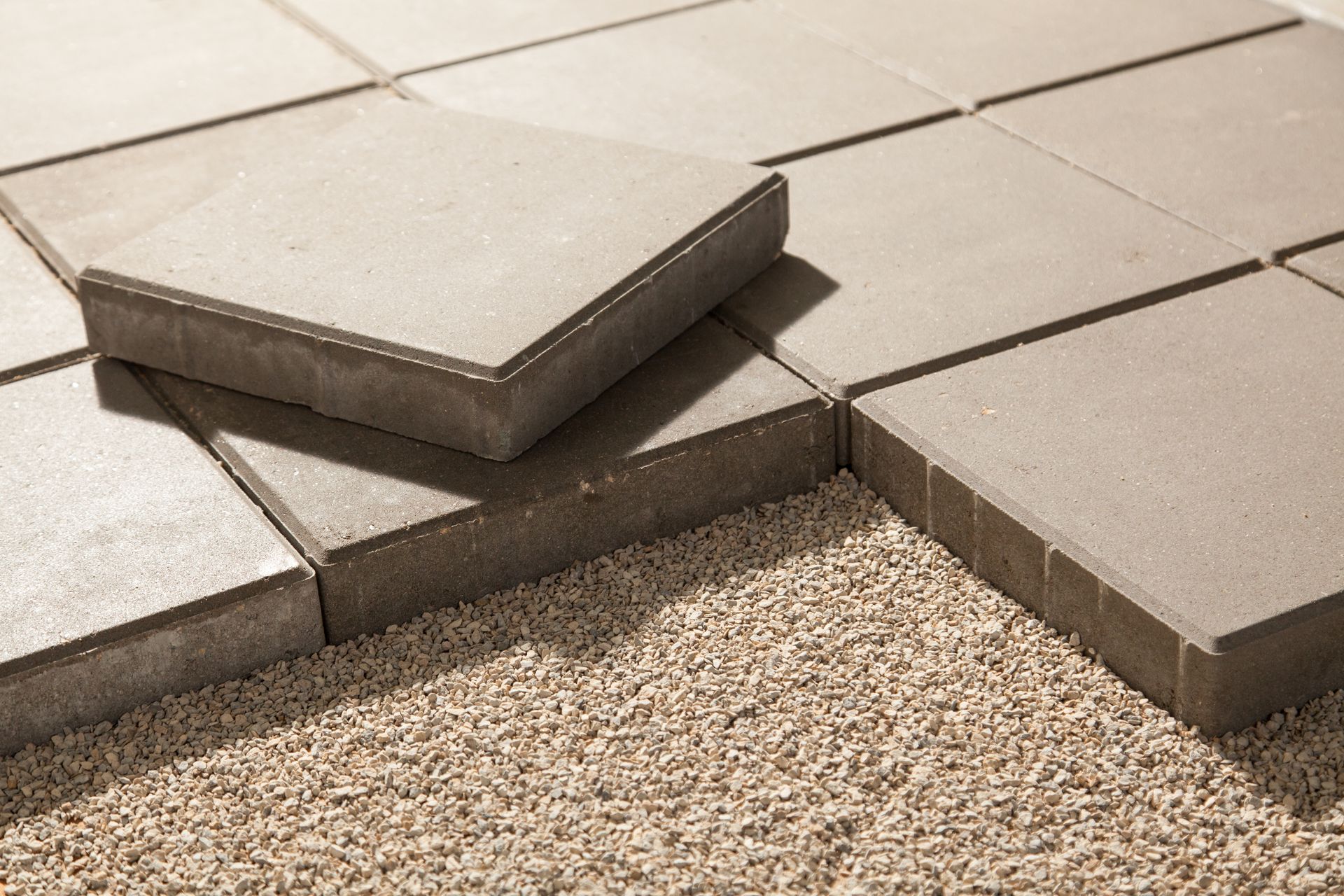 Gray paving stones being laid on a bed of gravel.