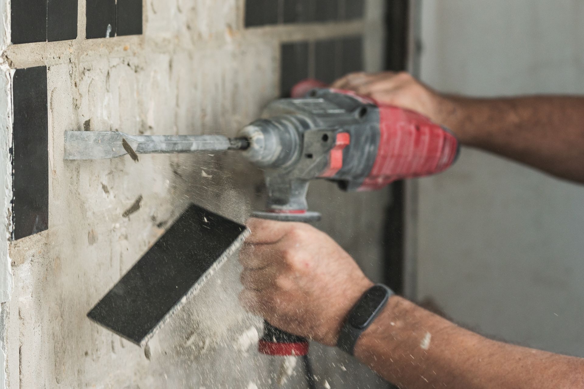 Person drilling into a wall, holding a drill and scraper, creating dust.