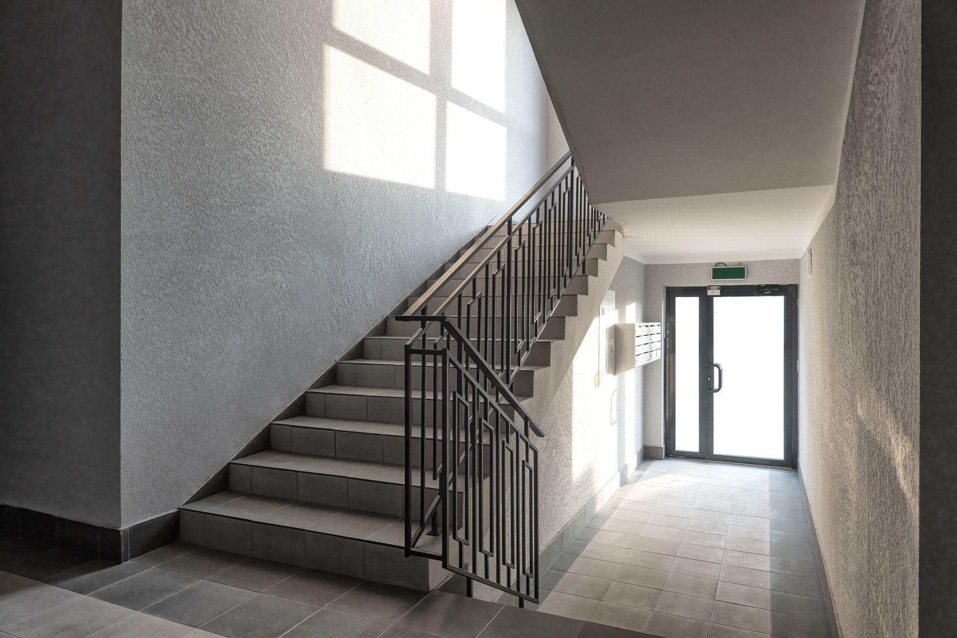 Stairwell with concrete steps, black railing, and exit door with light shining through.