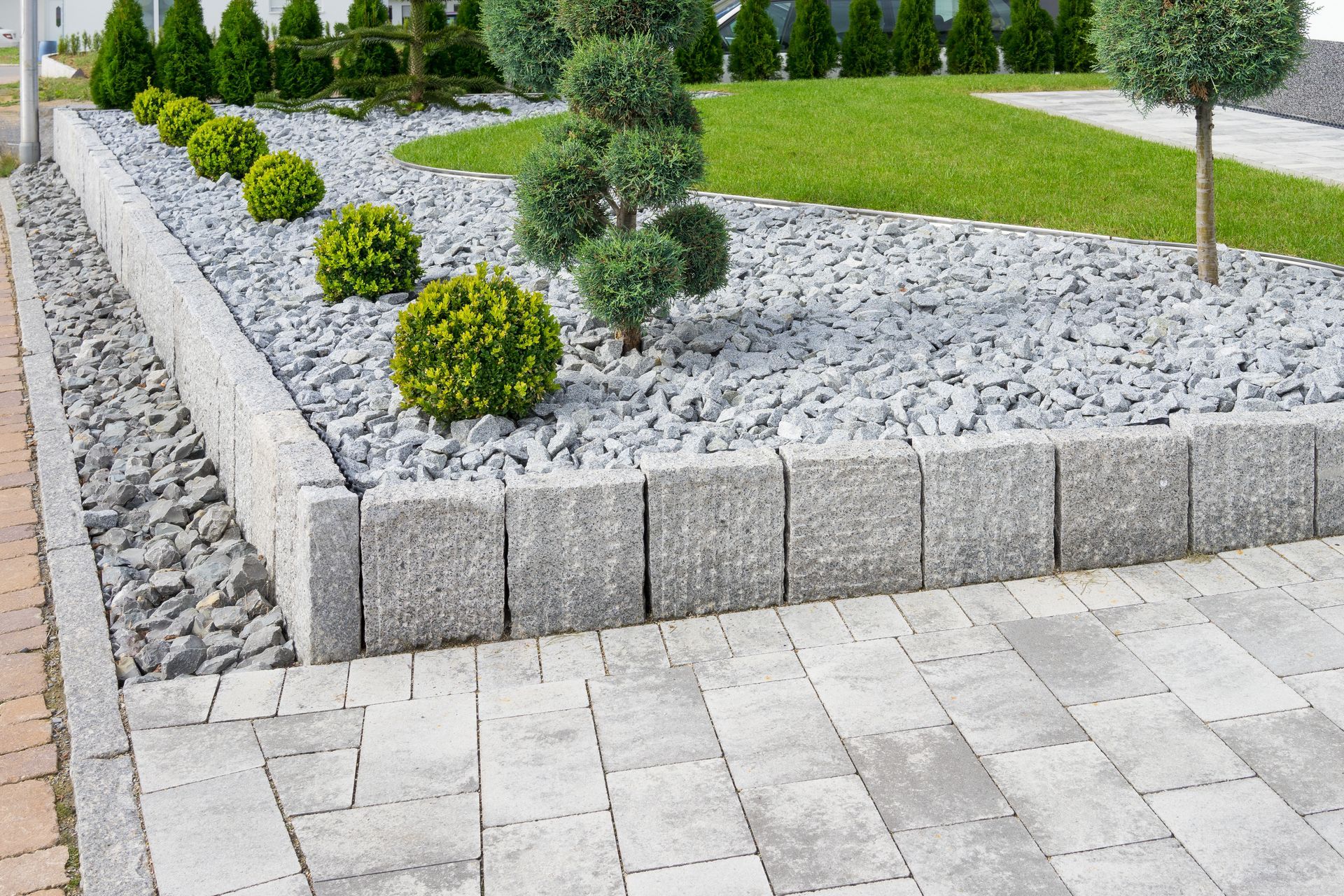 Gray stone retaining wall with shrubs, gravel, and green lawn.