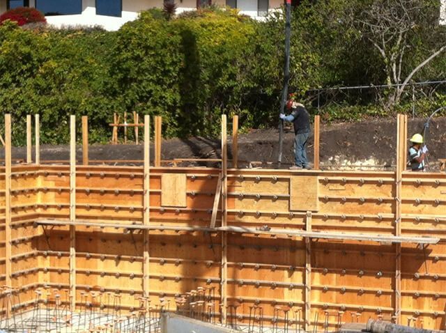 Construction workers pouring concrete into wooden forms at a construction site.
