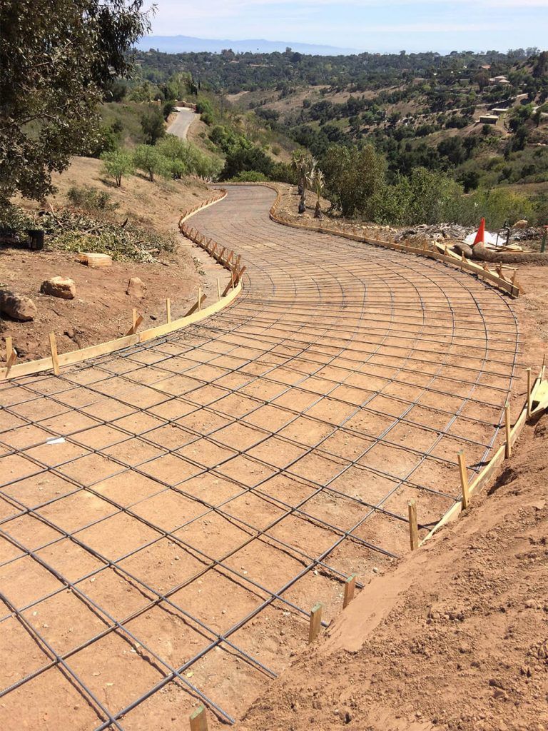 Road under construction with rebar grid laid on dirt surface.