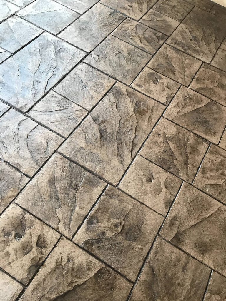 Close-up of stamped concrete flooring with stone-like texture, varying shades of gray.