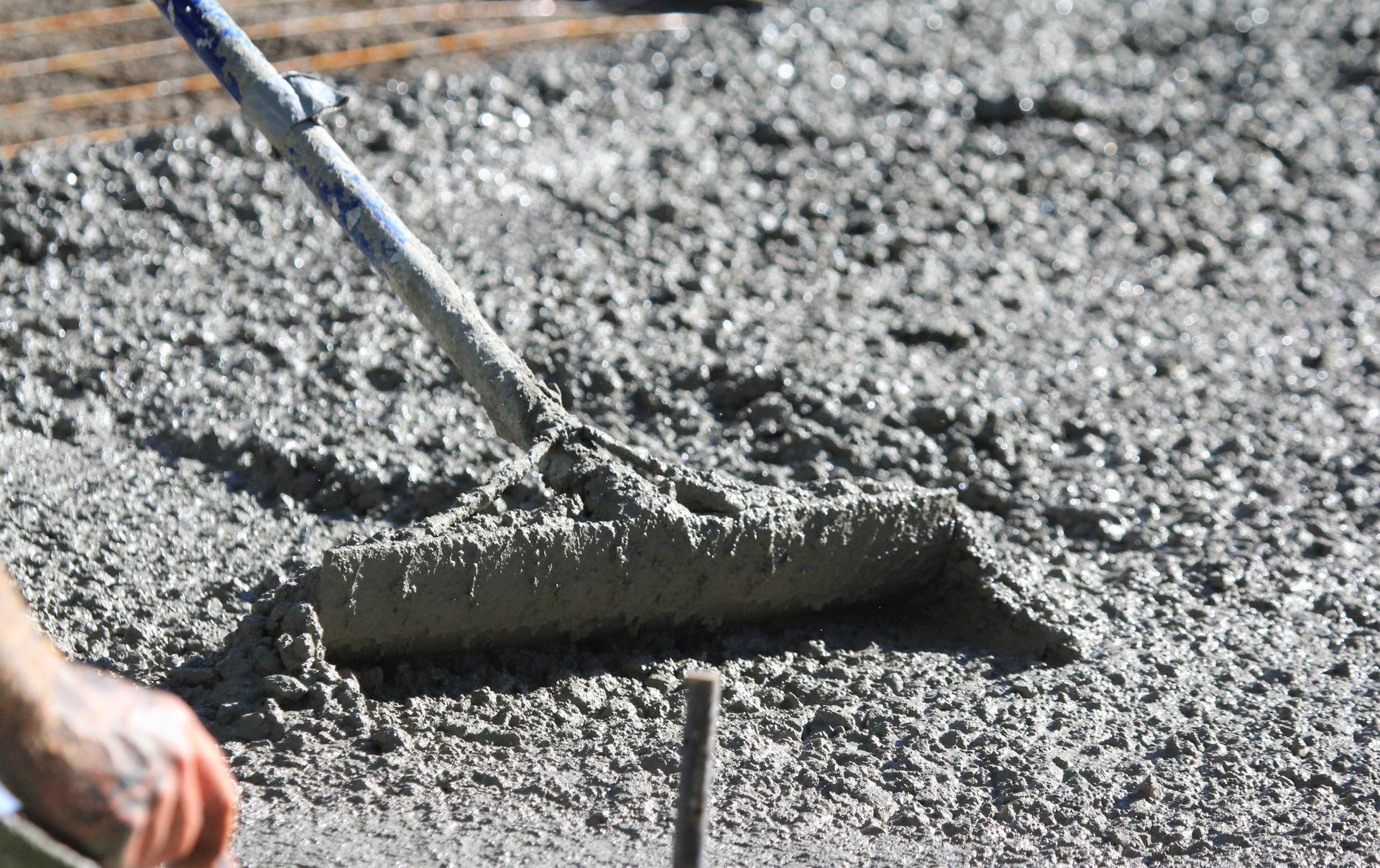 Person using a concrete rake to smooth wet cement on a construction site.
