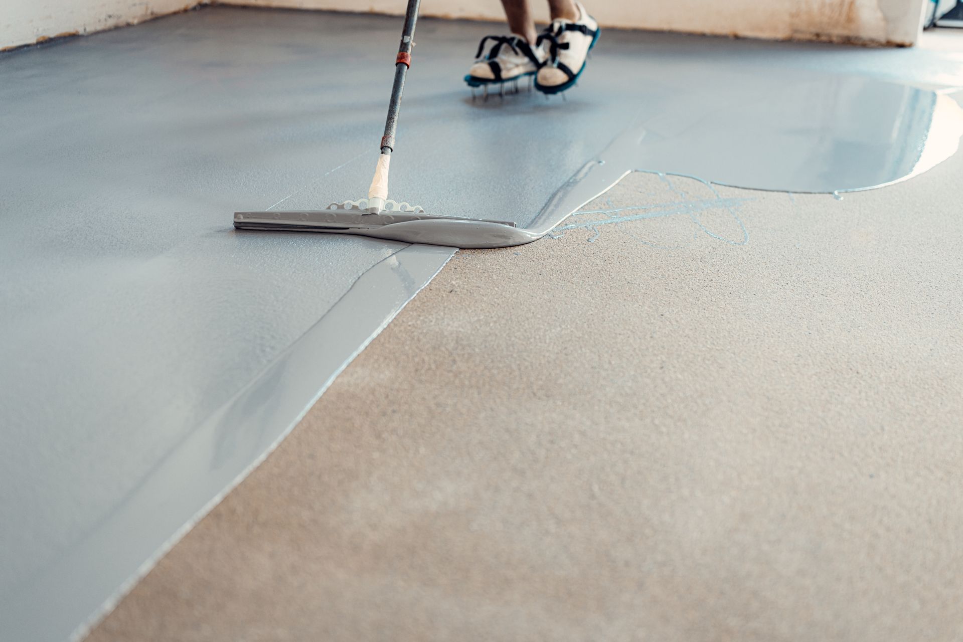 Person applying gray epoxy coating to a concrete floor with a squeegee.
