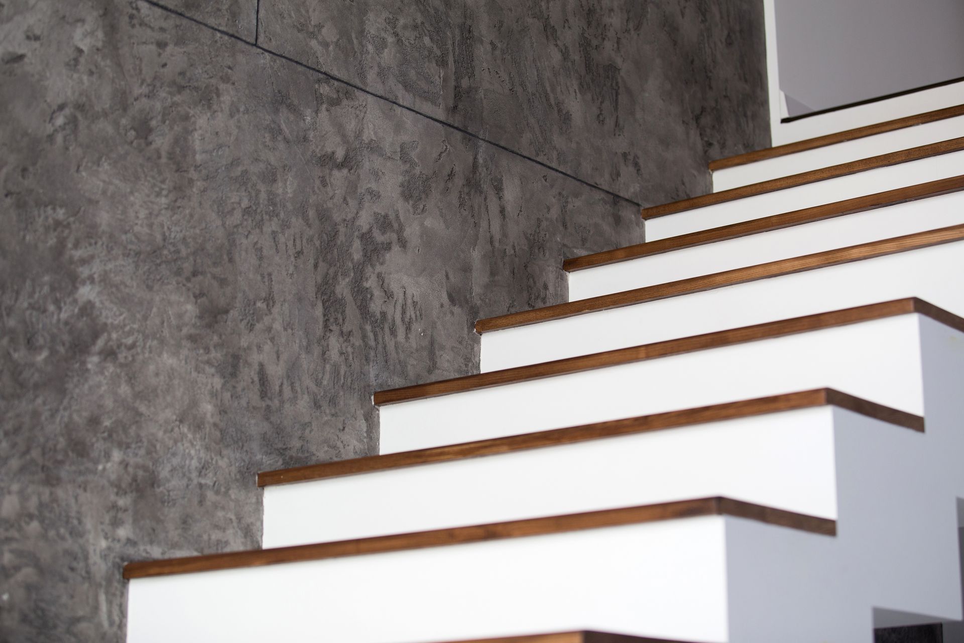 White staircase with brown wood treads against a textured gray wall.