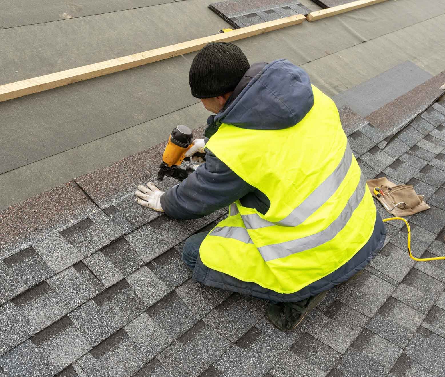 A man in a yellow vest is working on a roof.