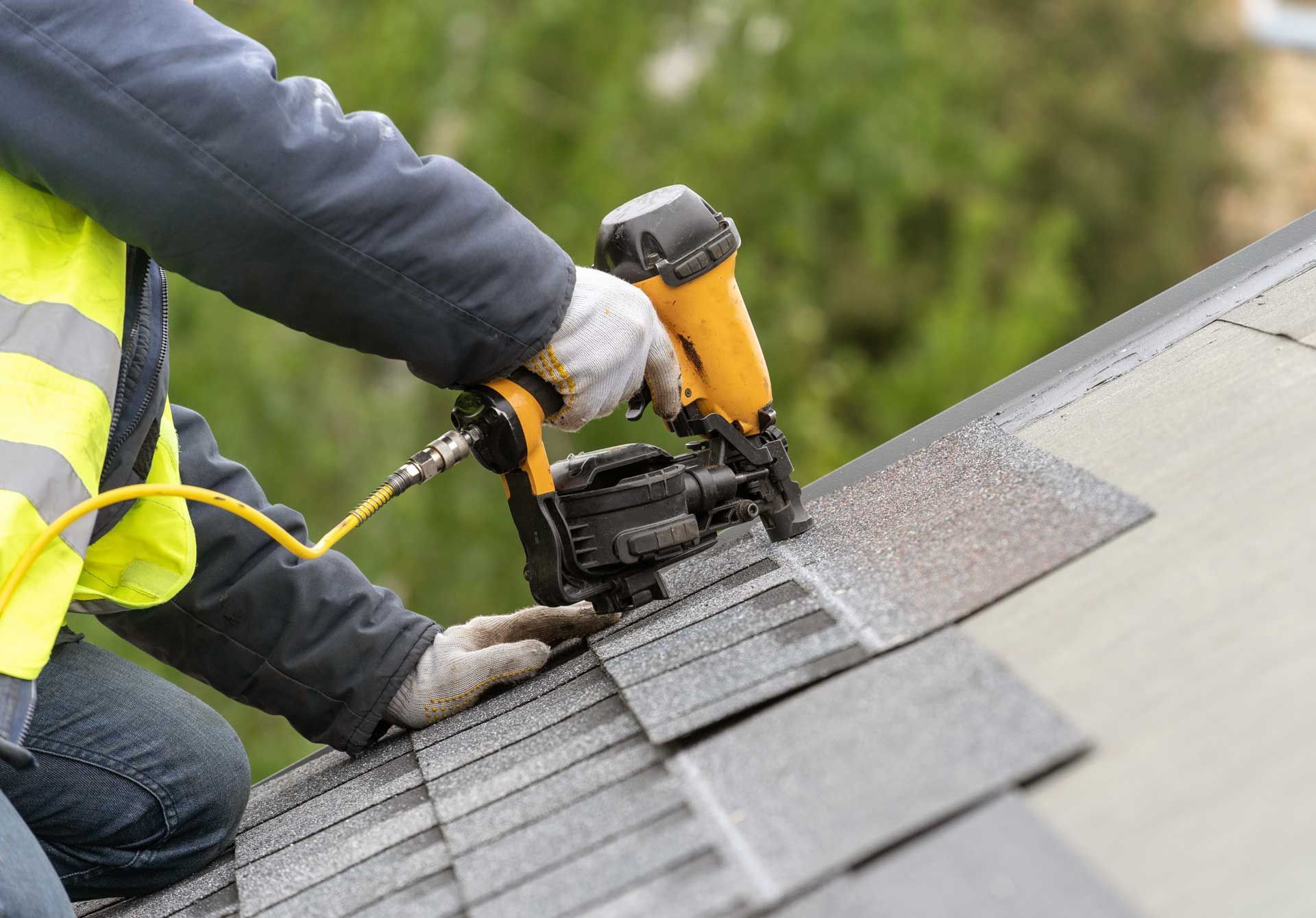 Workman using pneumatic nail gun install tile on roof