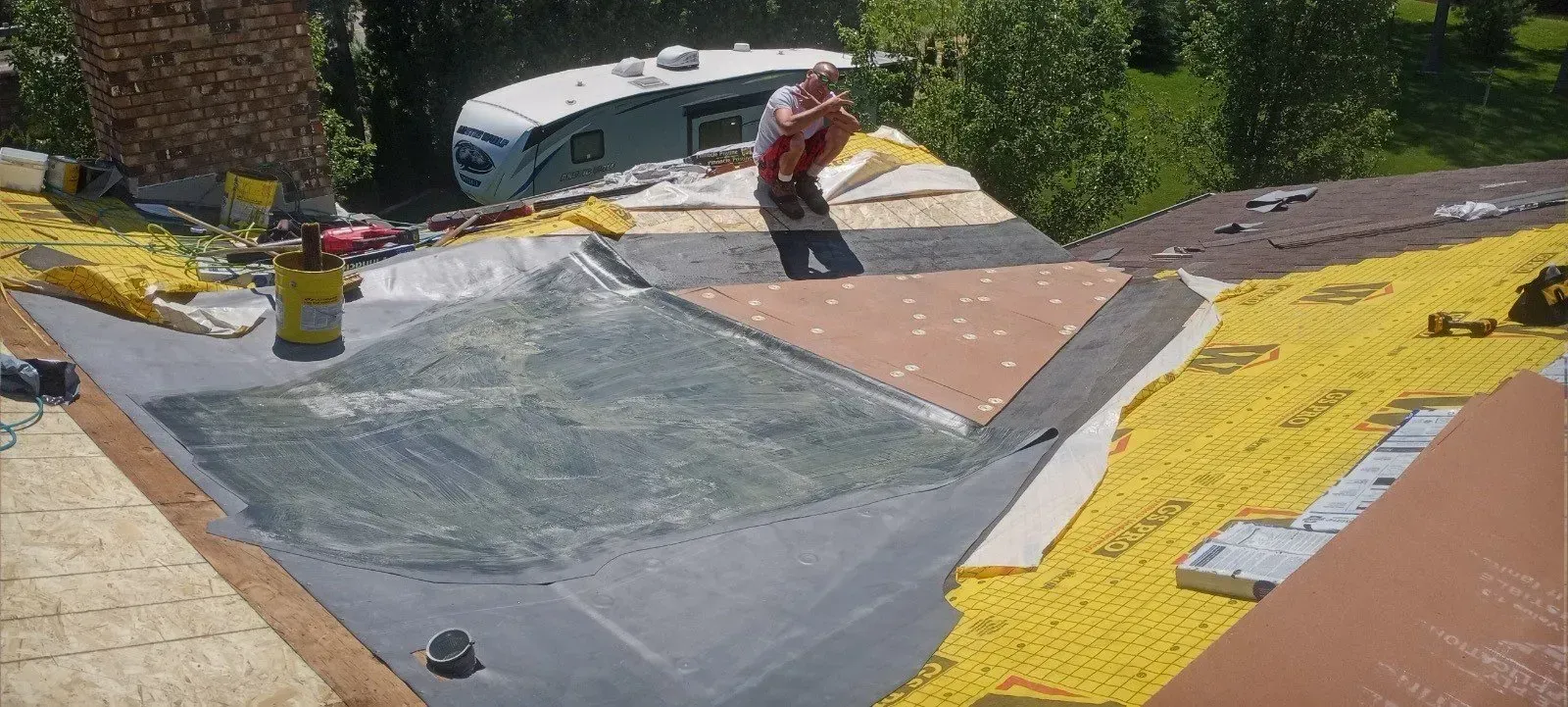 A man is working on a roof with a trailer in the background.