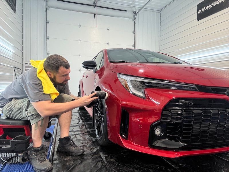 A man is polishing a red car in a garage.