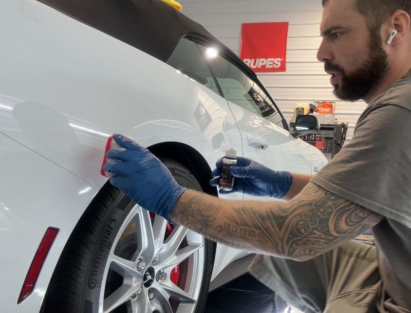 A man is polishing the fender of a white car.