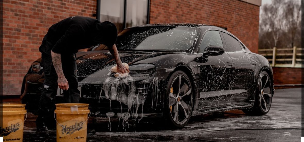 Person washing a black car with suds in front of a brick building.
